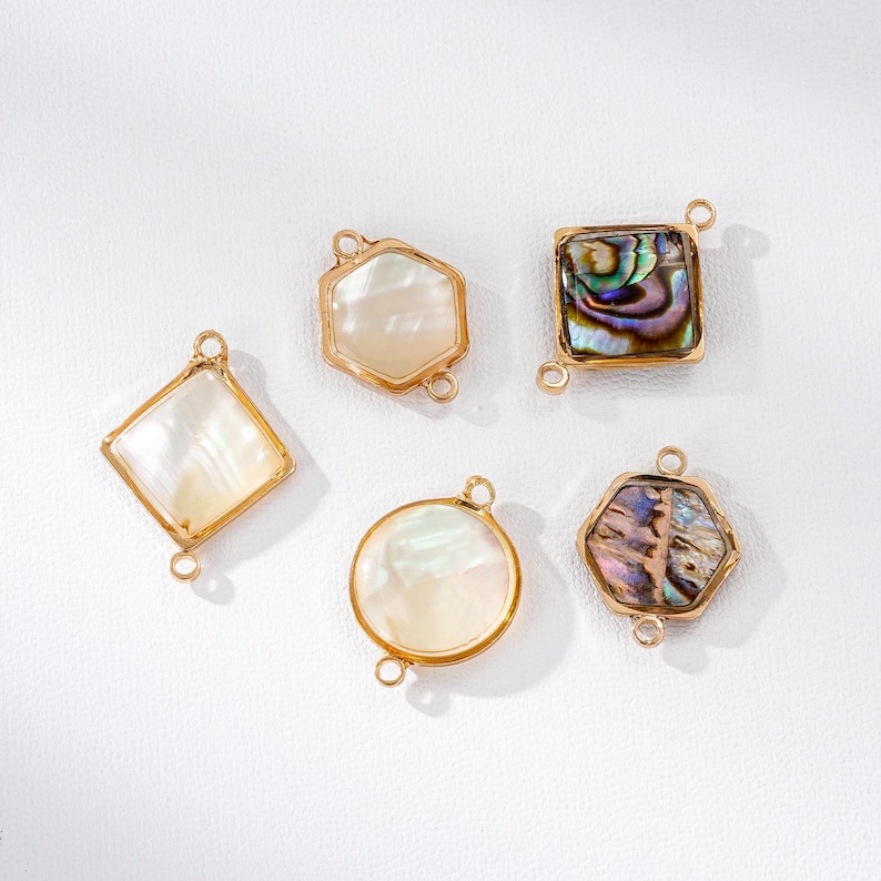 May include: Five gold-toned jewelry pendants in various shapes: a diamond, a hexagon, a square, a circle, and another hexagon. Each pendant features a mother-of-pearl or iridescent abalone shell inlay. The pendants have small loops for attaching to a chain or other jewelry components.