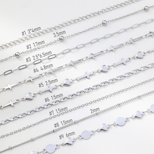May include: A collection of nine silver-colored chain necklaces, each with a unique design. The chains vary in style, including ball, oval link, cross, heart, and disc shapes. Measurements are provided for each chain, ranging from 1.5mm to 6mm in width.