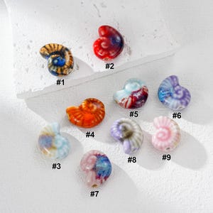Puede incluir: Nueve cuentas de cerámica con forma de concha en varios colores, numeradas y con acabado brillante. Los colores incluyen naranja, rojo, azul, morado y rosa. Adecuadas para la creación de joyas o proyectos de artesanía.