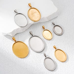 Könnte beinhalten: Eine Auswahl an ovalen Anhänger-Tabletts in Gold- und Silbertönen. Die Anhänger haben oben eine Schlaufe für eine Kette. Die Tabletts sind leer und bereit für die individuelle Gestaltung mit Harz, Fotos oder anderen Verzierungen.