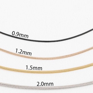 May include: Four snake chains of different thicknesses, from 0.9mm to 2.0mm, laid out on a white surface. The chains are black, rose gold, gold, and silver.