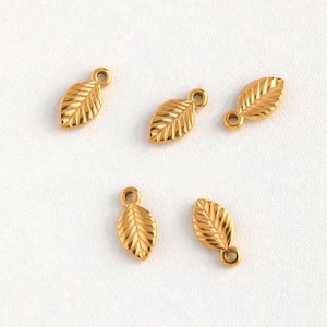 May include: Five gold leaf charms with a textured surface. Each charm has a small loop at the top for attaching to jewelry or other crafts.