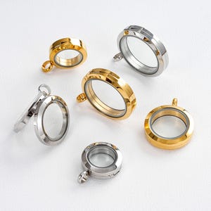 Peut inclure: Plusieurs pendentifs ronds en forme de médaillon en verre transparent, de couleurs or et argent. Chaque pendentif est doté d'une petite boucle pour l'attacher à une chaîne. Les médaillons sont vides.