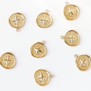 May include: Eight gold compass charms with a star design. The charms are round and have a hole at the top for attaching to a necklace or bracelet.