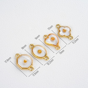 Pu&ograve; includere: Quattro ciondoli dorati a forma di charm in varie forme: un ottagono (17,8 mm x 11,5 mm), un ovale (18 mm x 10,2 mm), un cuore (16 mm x 11 mm) e un fiore a quattro petali (17 mm x 11,2 mm). Ogni ciondolo presenta un centro trasparente con un piccolo accento giallo rotondo.