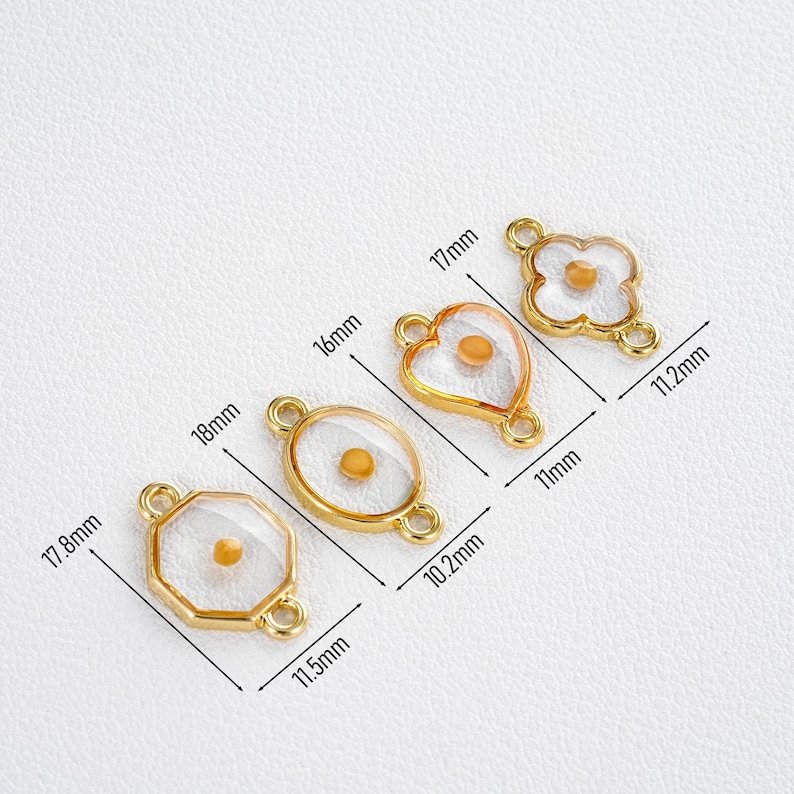 Pu&ograve; includere: Quattro ciondoli dorati a forma di charm in varie forme: un ottagono (17,8 mm x 11,5 mm), un ovale (18 mm x 10,2 mm), un cuore (16 mm x 11 mm) e un fiore a quattro petali (17 mm x 11,2 mm). Ogni ciondolo presenta un centro trasparente con un piccolo accento giallo rotondo.