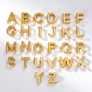 Op de afbeelding: Een verzameling goudkleurige alfabetletters, van A tot Z, gerangschikt op een witte ondergrond. Elke letter is een vet, driedimensionaal ontwerp dat licht reflecteert. De letters zijn gelijkmatig verdeeld.