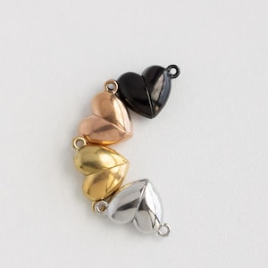 May include: Four heart-shaped magnetic clasps in different colours: black, rose gold, gold, and silver. The clasps are arranged in a semi-circle.