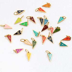 Op de afbeelding: Een verzameling goudkleurige hartvormige bedels, elk met een andere letter van het alfabet in verschillende kleuren. De bedels hebben een gouden lus aan de bovenkant om aan een ketting of armband te bevestigen.