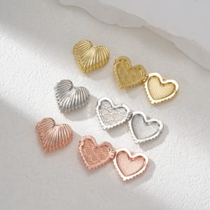 Puede incluir: Un conjunto de ocho dijes de corazón en forma de corazón en varios acabados, incluyendo oro, plata y oro rosa. Los dijes están abiertos para revelar un interior en blanco, perfecto para agregar un toque personal.