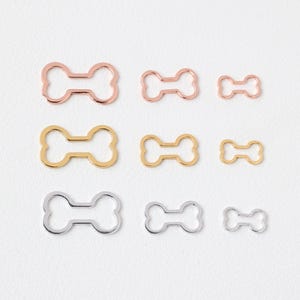 May include: Assortment of six bone-shaped metal charms in three different sizes. The charms are in silver, gold, and rose gold.