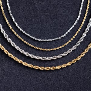 Puede incluir: Cuatro cadenas de cuerda diferentes, dos plateadas y dos doradas, se colocan sobre una superficie gris oscuro. Las cadenas están dispuestas en semicírculo, con la cadena más grande en la parte inferior y la más pequeña en la parte superior.