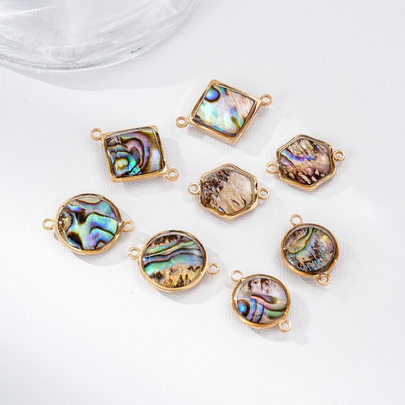 May include: A collection of iridescent abalone shell pendants in various shapes, including round, square, and hexagonal, set in gold-colored metal frames. Each pendant has small loops for attaching to jewelry.