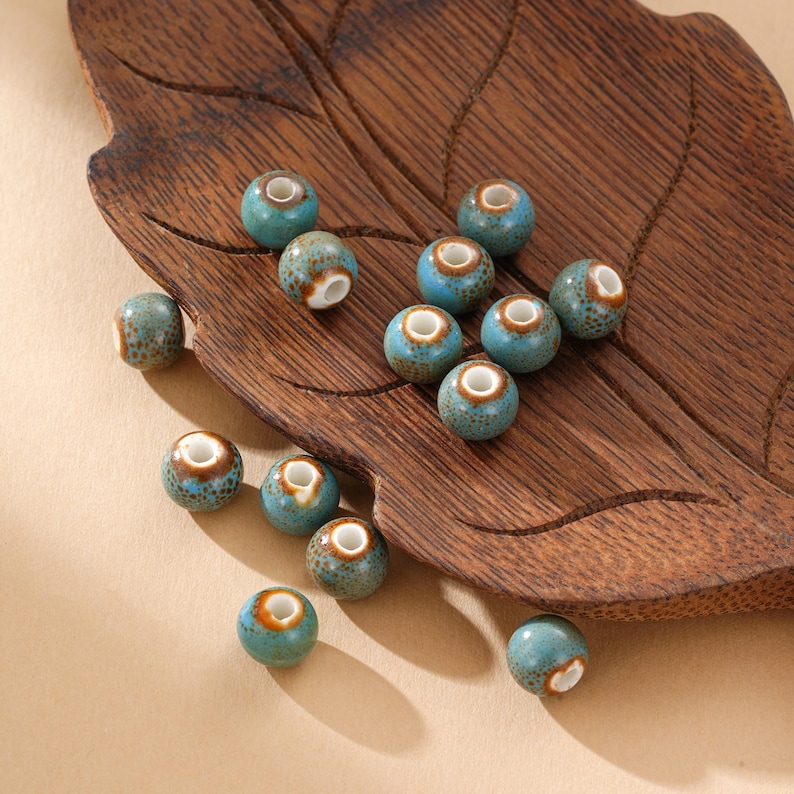 May include: A collection of turquoise ceramic beads with brown and white accents. The beads are round with a hole through the center, and are displayed on a wooden leaf-shaped tray. These beads are suitable for jewelry making and crafts.