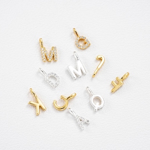 Puede incluir: Una colección de colgantes de alfabeto dorados y plateados. Los colgantes incluyen las letras M, G, D, K, J, Q, F, A y M. Algunos colgantes están incrustados con pequeñas piedras preciosas transparentes. Los colgantes están diseñados para la fabricación de joyas.