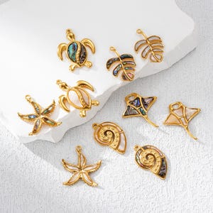 Può includere: Una collezione di ciondoli dorati a forma di creature marine: tartarughe, stelle marine, foglie, razze e conchiglie. Ogni ciondolo presenta dettagli iridescenti di conchiglia di abalone, aggiungendo colore e brillantezza. Ideale per la creazione di gioielli.
