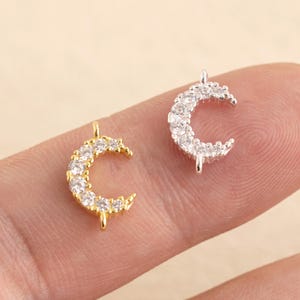 Puede incluir: Dos dijes de media luna con detalles de cristal transparente. Un dije es dorado y el otro es plateado.