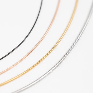 May include: Four different chain necklaces in black, rose gold, gold, and silver. The chains are all the same style, a thin, delicate snake chain.