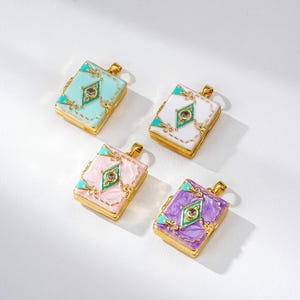 Puede incluir: Cuatro colgantes con forma de libro en colores pastel: azul claro, blanco, rosa y morado. Cada uno tiene un borde dorado y un diseño central en forma de diamante con una gema y detalles turquesa. Miden aproximadamente 2,5 cm de largo.