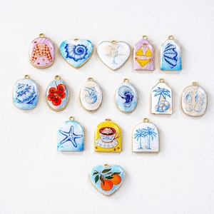 May include: A collection of colorful enamel charms with gold-tone edges. The charms feature various designs, including a seashell, a cocktail, a bikini, a starfish, a coffee cup, and a pair of flip-flops. The charms are in various shapes, including oval, heart, and tag shapes.