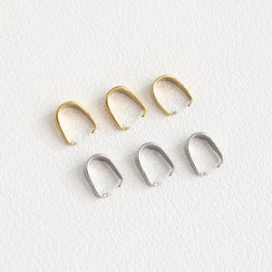 May include: Six metal jewellery clasps, three gold and three silver, in a close-up view. The clasps are small and round, with a slight opening at the top.
