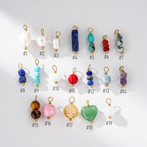 May include: Nineteen gemstone and pearl charms with gold-tone loops are displayed. The charms showcase diverse shapes and colours, such as white pearls, blue lapis lazuli, red beads, and green jade. Each charm is numbered for easy reference.