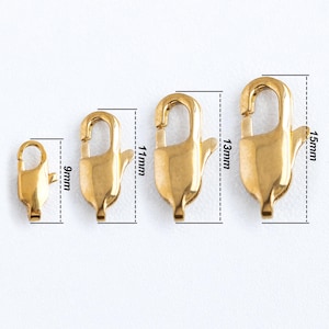 Könnte beinhalten: Vier goldfarbene Hummerverschlüsse in verschiedenen Größen: 9 mm, 11 mm, 13 mm und 15 mm. Die Verschlüsse werden vor einem weißen Hintergrund gezeigt.