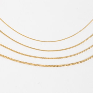 May include: Four gold snake chains of different lengths on a white background.