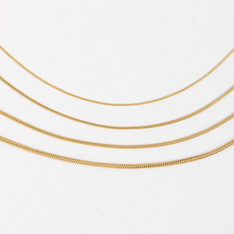 May include: Four gold snake chains of different lengths on a white background.