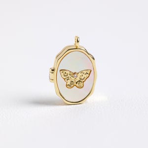 May include: A gold oval locket with a white mother-of-pearl inlay featuring a gold butterfly with a small diamond accent.