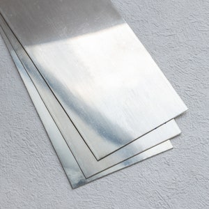 May include: Three sheets of silver metal stacked on top of each other. The metal is shiny and reflective.