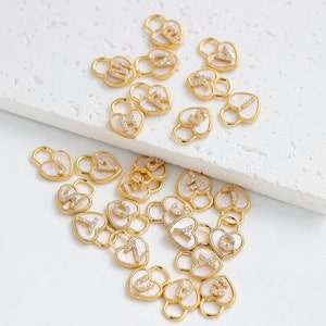 Op de afbeelding: Een verzameling van hartvormige gouden bedels met een witte emaille afwerking en een enkele letter in pavé diamanten op elke bedel.