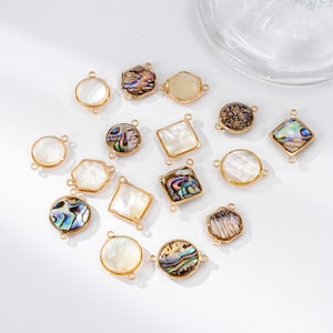 May include: A collection of gold-toned jewelry components in various shapes, including circles, squares, hexagons, and irregular forms. Some pieces feature iridescent abalone shells, while others have a pearly white appearance. The components are designed with small loops for attachment.