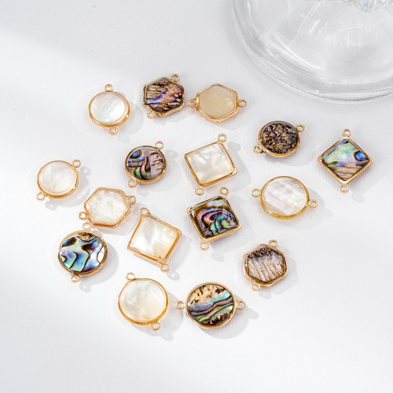 May include: A collection of gold-toned jewelry components in various shapes, including circles, squares, hexagons, and irregular forms. Some pieces feature iridescent abalone shells, while others have a pearly white appearance. The components are designed with small loops for attachment.