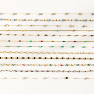 Könnte beinhalten: Eine Sammlung von 10 goldenen Kettenhalsketten mit verschiedenen farbigen Perlen. Die Perlen sind blau, weiß, rot, grün, gelb und schwarz. Einige der Halsketten haben böse Augenperlen.