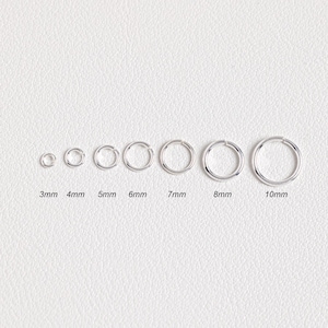 May include: A set of eight silver jump rings in various sizes, ranging from 3mm to 10mm in diameter. The rings are arranged in order of size, with the smallest ring on the left and the largest ring on the right.