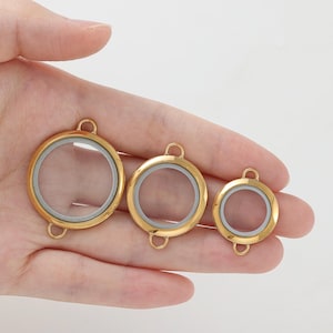 Peut inclure: Trois médaillons ronds dorés avec des centres en verre transparent. Chaque médaillon a une petite boucle en haut et en bas pour l'attacher à une chaîne. Les médaillons sont de tailles variables, le plus grand étant à gauche.