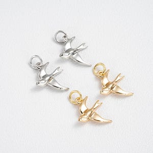 Könnte beinhalten: Vier vogelformige Anhänger in Gold- und Silberfarben. Jeder Anhänger hat oben eine kleine Schlaufe zum Befestigen an einer Halskette oder einem Armband. Die Anhänger sind mit Flügeln und einem stromlinienförmigen Körper versehen.