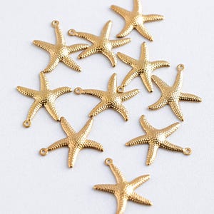 Op de afbeelding: Tien gouden metalen zeesterren bedels. De bedels zijn ongeveer 2,5 cm groot en hebben een getextureerd oppervlak.