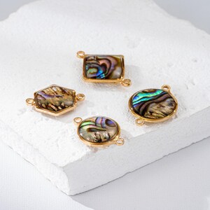 May include: Four gold-toned jewelry components with iridescent abalone shell inlays. The shapes include a rectangle, hexagon, and two circles. Each piece has small loops for attaching to other jewelry elements. The abalone shells display a range of colors.