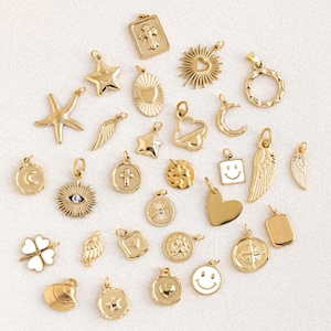 Può includere: Una collezione di 27 ciondoli dorati con vari design, tra cui stelle, cuori, croci, lune, nuvole, facce sorridenti e altro ancora. I ciondoli sono disposti su una superficie bianca.