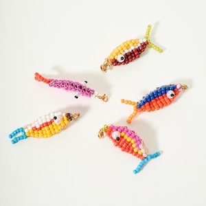 Könnte beinhalten: Fünf Perlenfische in verschiedenen Farben, darunter Gelb, Rot, Rosa, Blau und Orange. Jeder Fisch hat ein einzigartiges Muster und Design mit goldfarbenen Akzenten und kleinen Perlenaugen. Die Fische sind auf weißem Hintergrund angeordnet.
