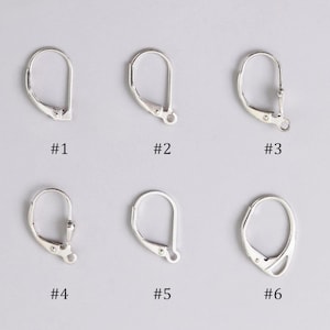 Puede incluir: Se muestran seis ganchos de pendientes plateados sobre un fondo claro. Cada gancho tiene un diseño diferente, con variaciones en las formas del cierre y del lazo. Los ganchos están etiquetados con números del #1 al #6.