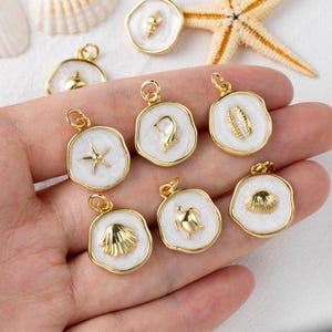 May include: A selection of gold-tone pendants featuring white enamel and marine motifs such as a starfish, seashell, and turtle. The pendants are presented against a plain backdrop, indicating a jewellery or craft focus.