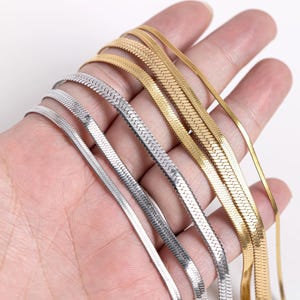 Könnte beinhalten: Nahaufnahme von fünf verschiedenen goldenen und silbernen Schlangenketten. Die Ketten sind fächerförmig angeordnet und werden in der Hand einer Person gehalten.