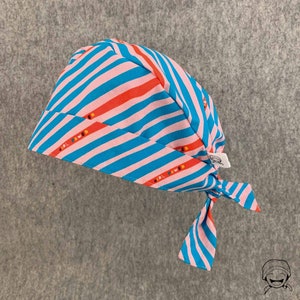May include: A blue and pink striped surgical cap with the text "Girl Power" repeated on the fabric. The cap has a tie at the back.