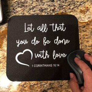 May include: Black mouse pad with white text that reads "Let all that you do be done with love 1 Corinthians 16:14". A white heart is above the text.