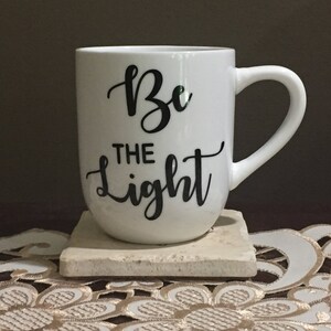 May include: White ceramic mug with a black inscription that reads "Be the light".