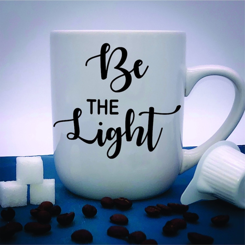 May include: White ceramic coffee mug with black text that reads "Be the Light".