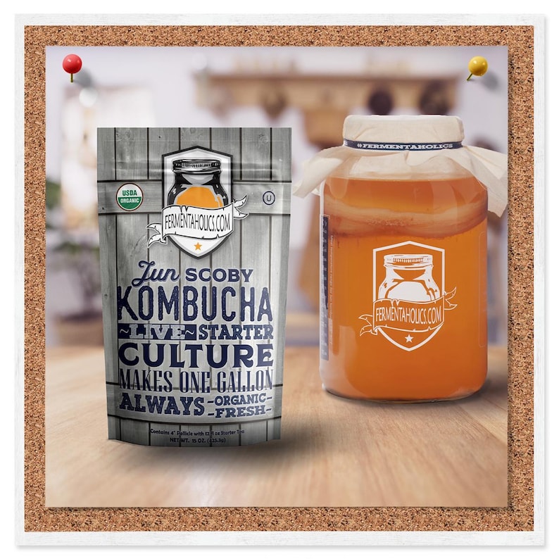 K&ouml;nnte beinhalten: Ein wei&szlig;er Beutel mit einem blauen und orangefarbenen Etikett, auf dem "Jun SCOBY Kombucha Live Starter Culture Makes One Gallon Always - Organic - Fresh -" steht. Der Beutel liegt auf einer Holzoberfl&auml;che neben einem durchsichtigen Glasgef&auml;&szlig; mit einem wei&szlig;en Stoffdeckel, gef&uuml;llt mit einer hellorangen Fl&uuml;ssigkeit. Das Gef&auml;&szlig; tr&auml;gt ein wei&szlig;es Etikett mit dem Text "FERMENTAHOLICS.COM".